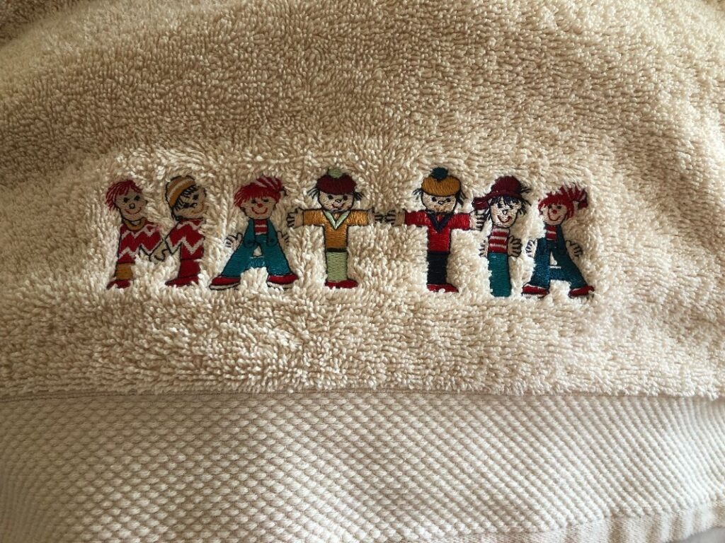 Serviette éponge brodée du prénom Mattia, où chaque lettre est accompagnée d'un petit personnage