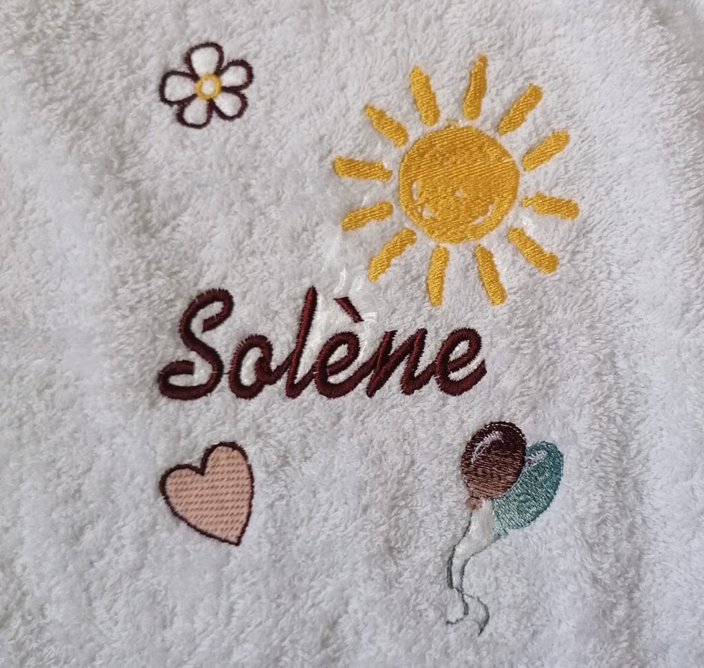 Serviette blanche brodée du prénom Solène, d'un soleil, d'une fleur, d'un cœur et de ballons
