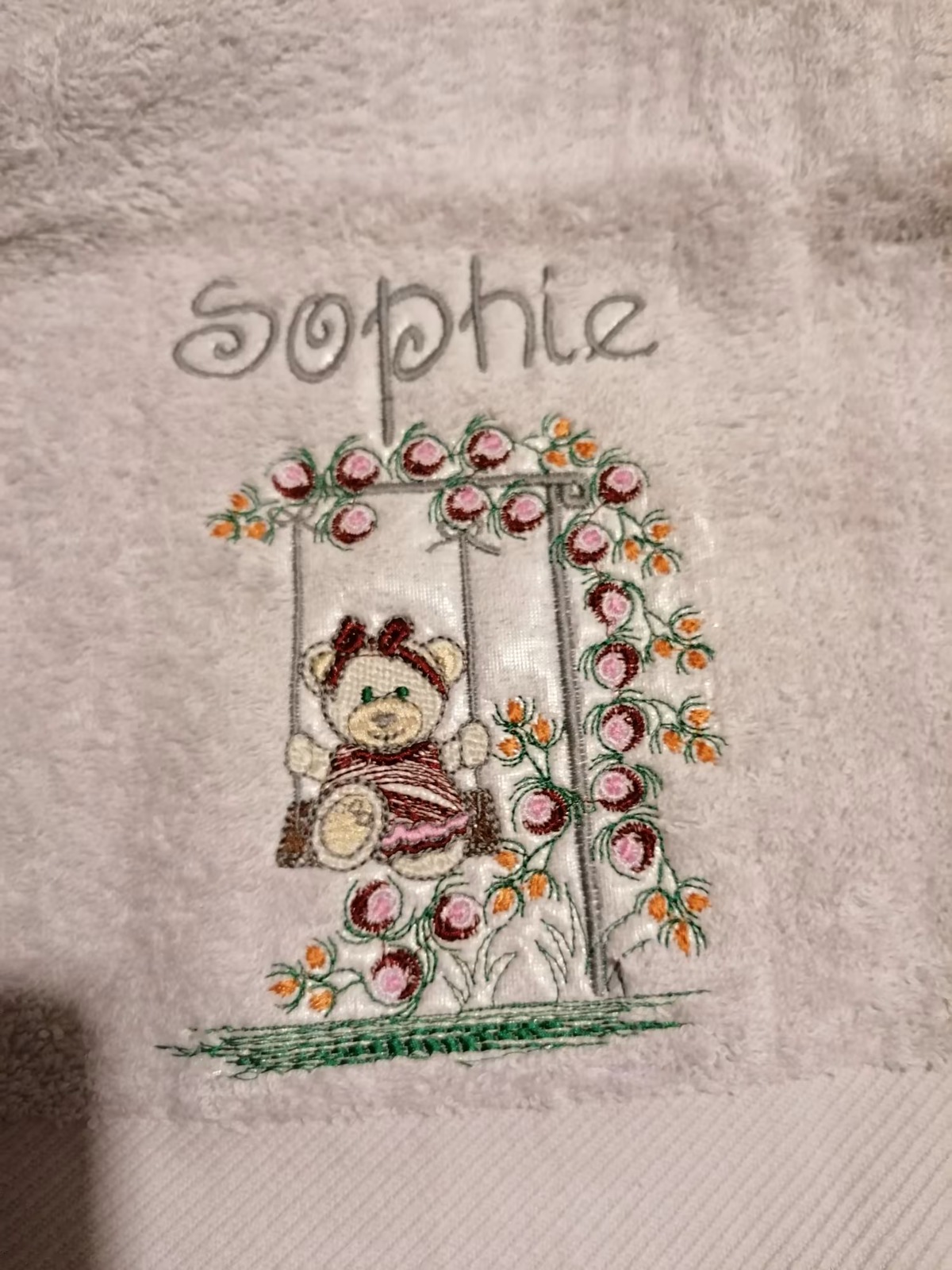 Serviette de toilette brodée du prénom Sophie et d'un ourson sur une balançoire fleurie
