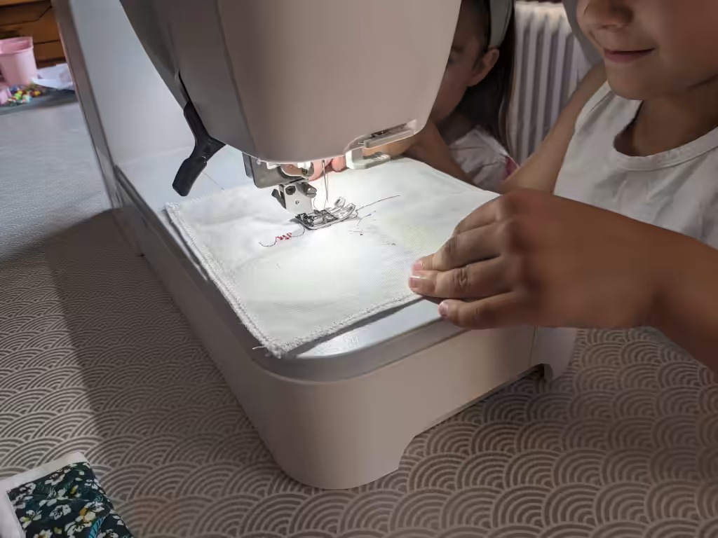 Une enfant guide un tissu sous l'aiguille d'une machine à broder