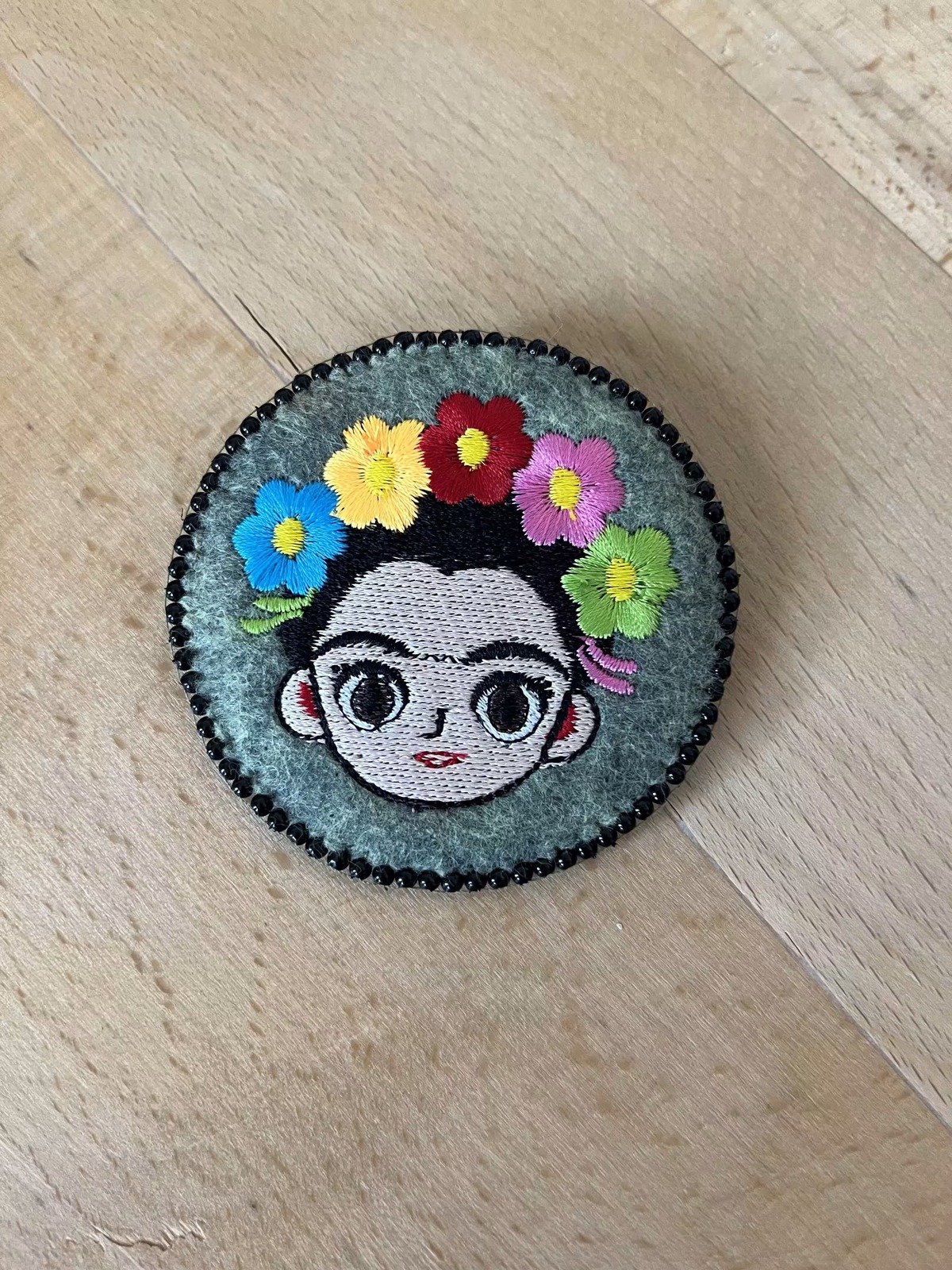 Broche ronde brodée d'un portrait de femme couronnée de fleurs